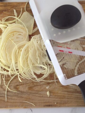 A chopping board, shredded cabbage and a mandolin.