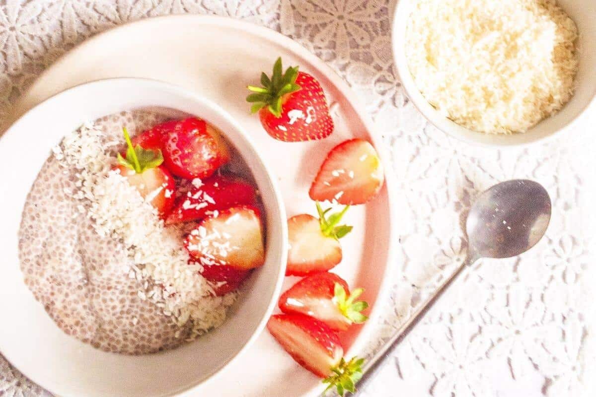 A bowl of creamy chia pudding sprinkled with coconut and halved fresh strawberries.
