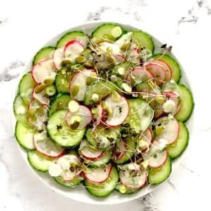 A bowl of sliced cucumbers with fresh sprouts, radish and seeds.
