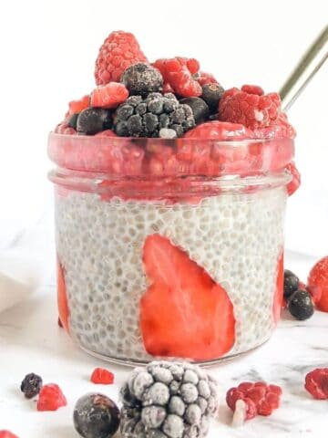 A small glass of chia pudding topped with fresh and frozen berries.