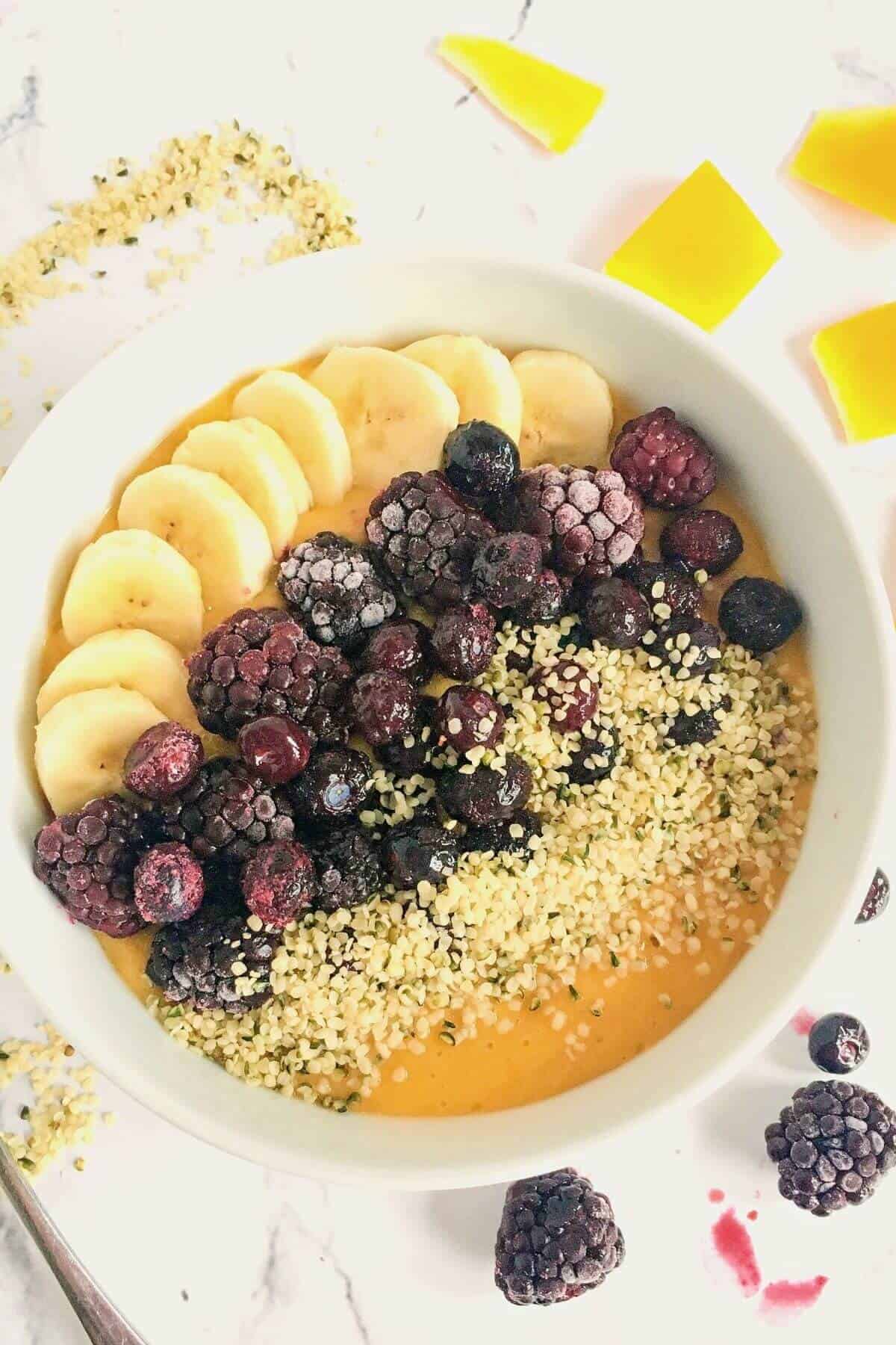 A bowl of mango smoothie topped with berries and hemp seeds.