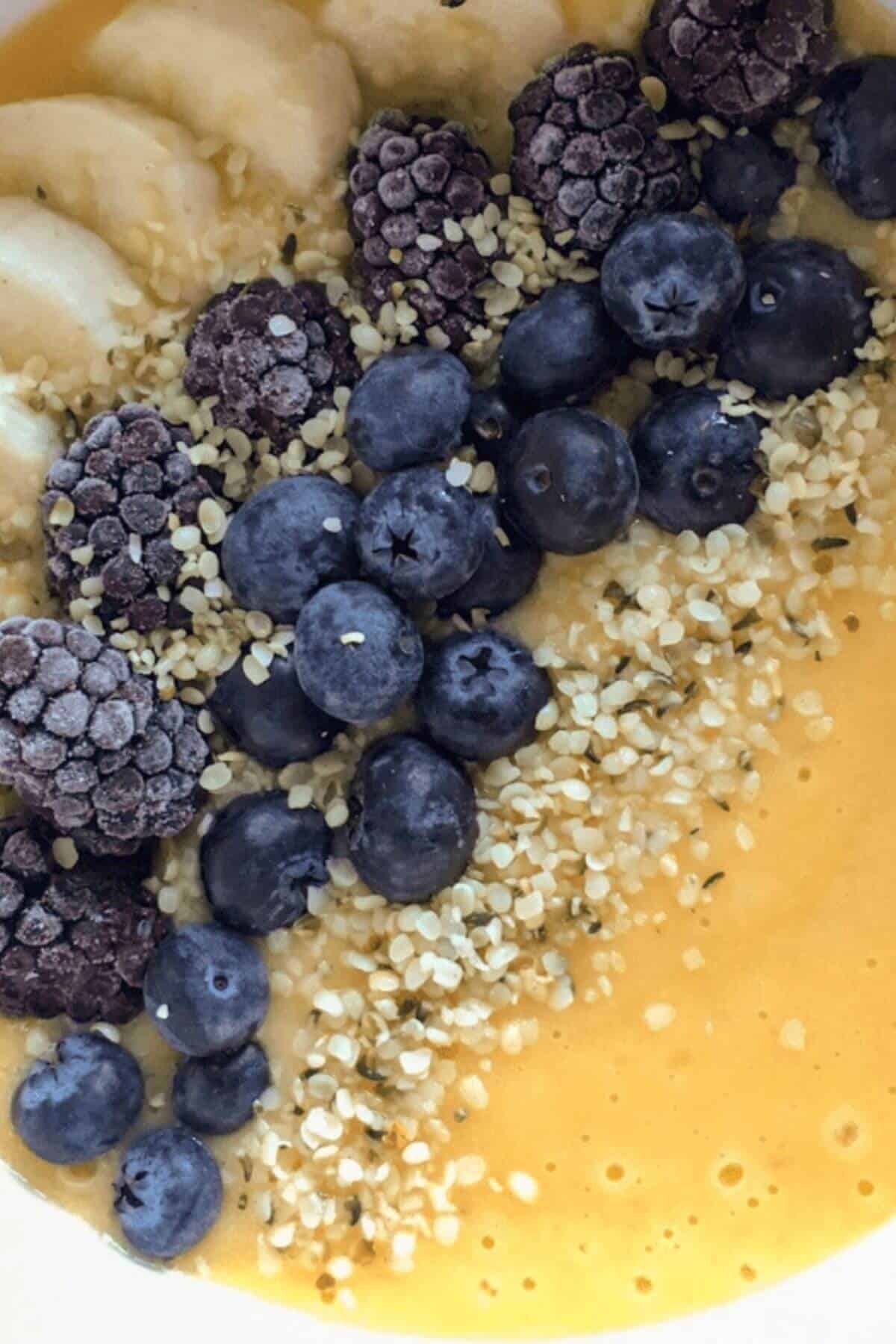 Close up of a smoothie topped with fresh berries, banana slices and hemp seeds.