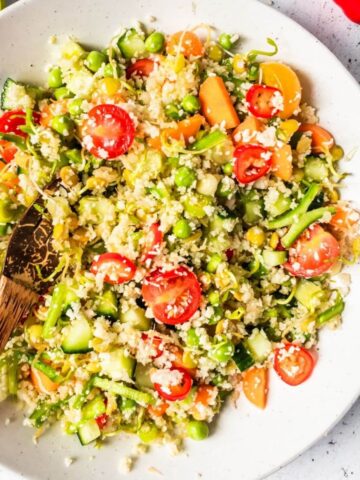 A bowl of cauliflower rice with diced vegetables, lentils and tomatoes.