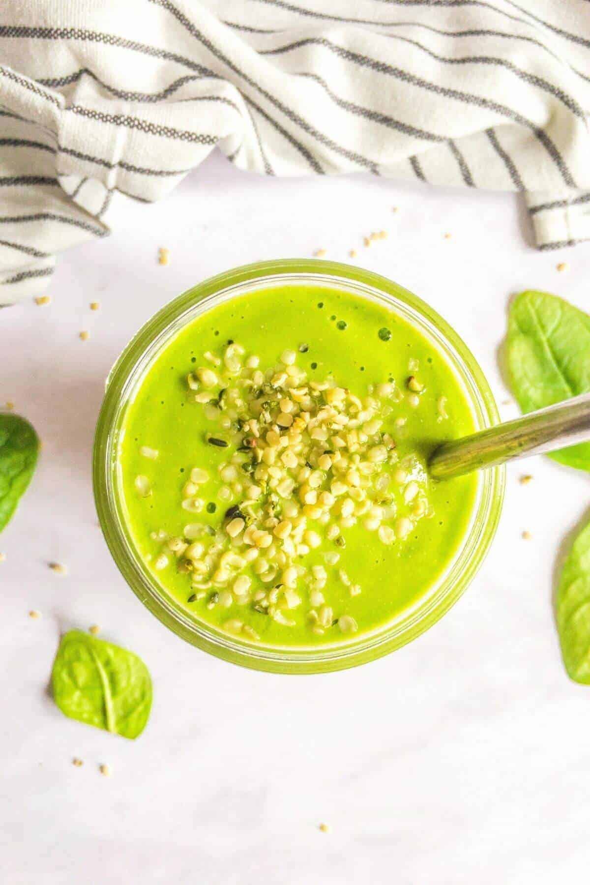 A bright green smoothie topped with hemp seeds and a straw.