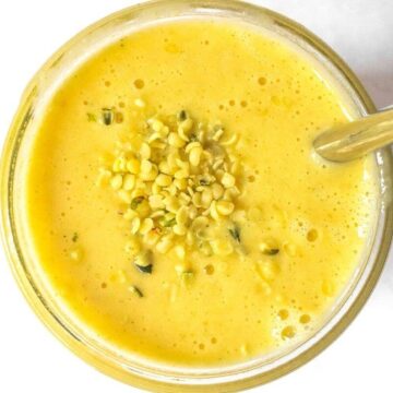 A glass filled with mango pineapple smoothie topped with hemp seeds.