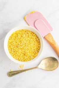 A small dish of vegan parmesan next to a pink spatula and silver spoon.