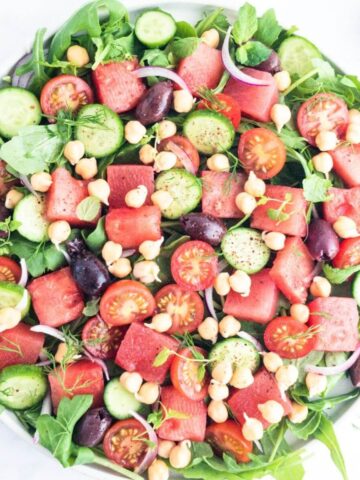 A large bowl of watermelon, chickpea and rocket salad with olives.