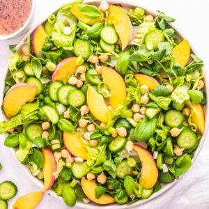 A large plate with peach and watercress salad with chickpeas and baby cucumber slices.
