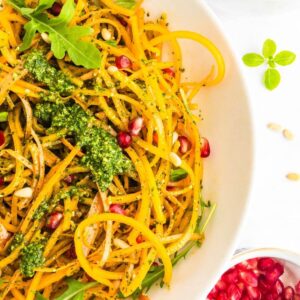 A bowl of butternut squash noodles with pesto and pomegranate seeds.