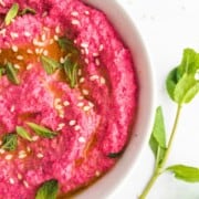Bright pink hummus in a small ceramic dish topped with fresh mint leaves.