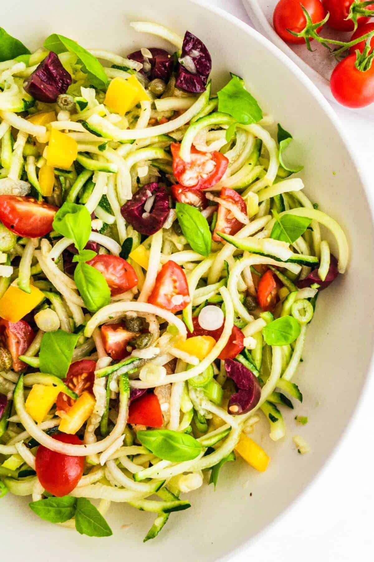 A bowl of courgette noodles mixed with diced mediterranean vegetables and basil leaves.
