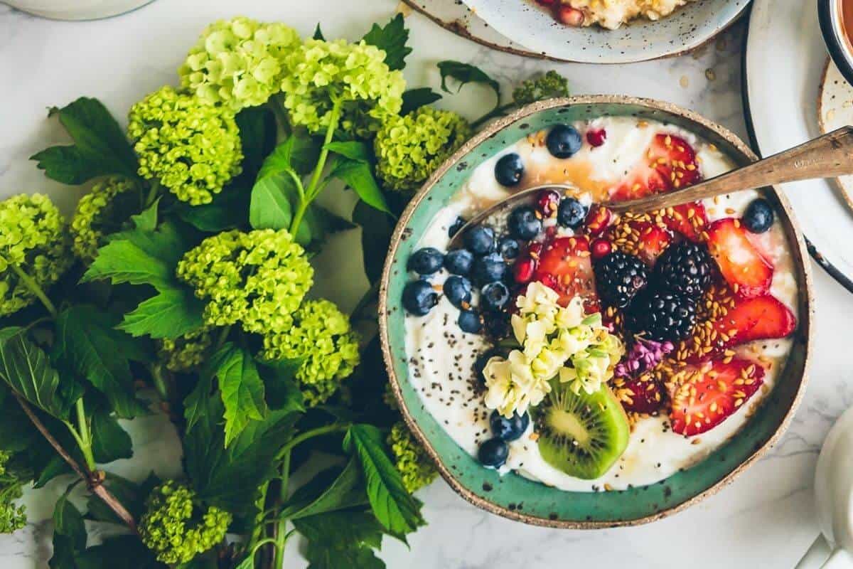 Breakfast bowl filled with fresh berries next to a bunch of green flowers.