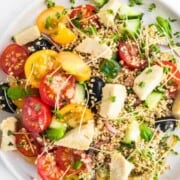 A plate of quinoa with cherry tomatoes, olives, cucumber, cheese and herbs.