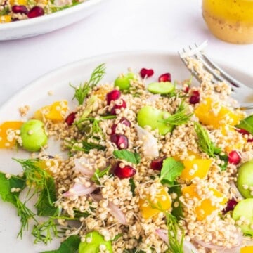 A plate of quinoa salad next to a glass containing dressing.