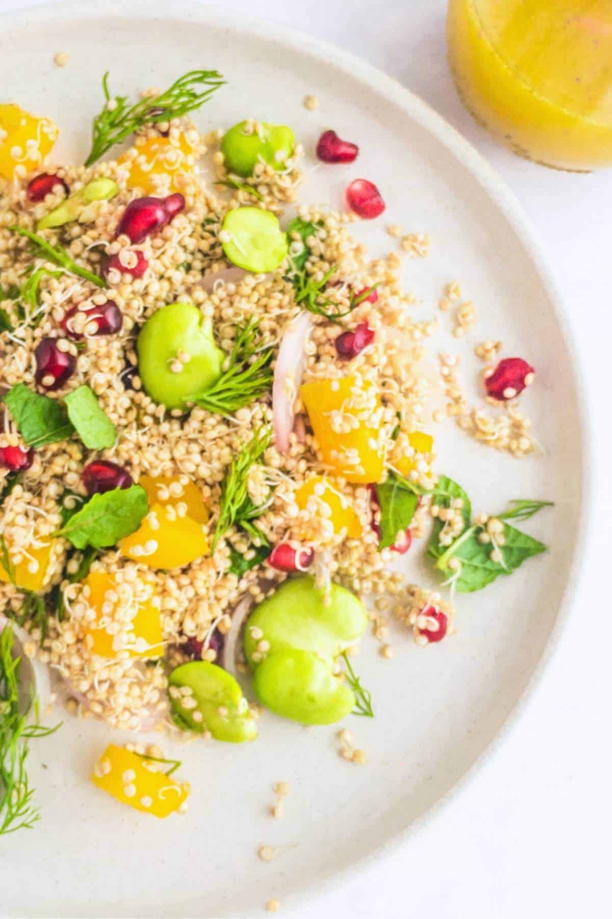 A plate of sprouted quinoa salad next to a glass with vinaigrette.