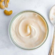 A small dish of thick, creamy mayonnaise with a few cashew nuts & a teaspoon on the side.