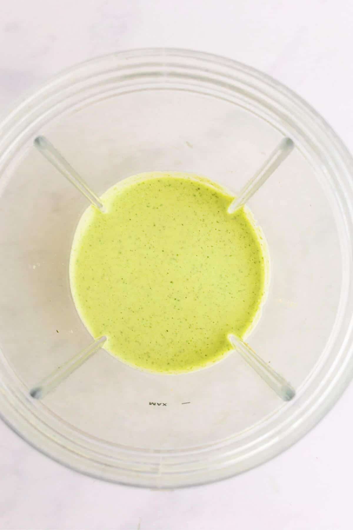 Close up of a green dressing in a blender cup.