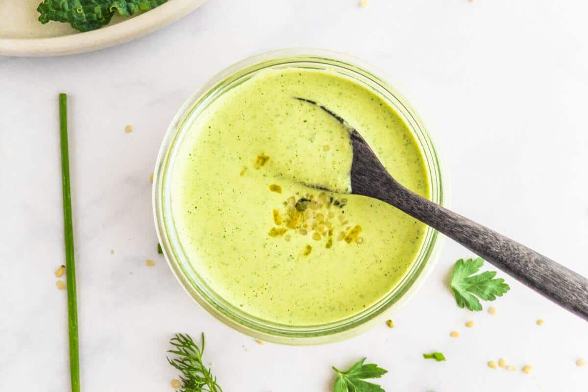 A sprinkling of fresh herbs and hemp hearts near a dish containing green dressing and a spoon.