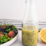 A bottle of salad vinaigrette with a salad and some fresh lemon.