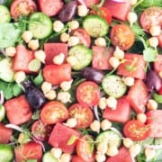 A plate of salad with green leaves, diced watermelon and chickpea sprouts.