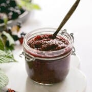 A jar of blackberry jam with a wooden teaspoon sticking out of the top.