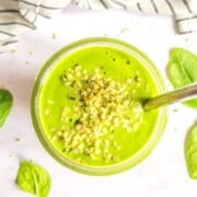 A glass of green smoothie topped with hemp seeds and a silver straw.