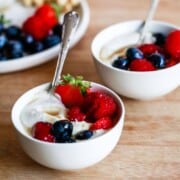 Two bowls filled with yogurt and fresh berries with silver spoons popping out of the top.