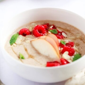 A bowl of porridge topped with raspberries, sliced pear and sprinkled with flaked almonds and mint leaves.