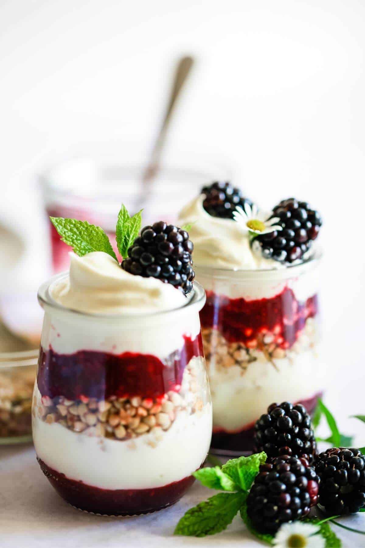 Two blackberry yogurt parfaits garnished with mint and daisies.