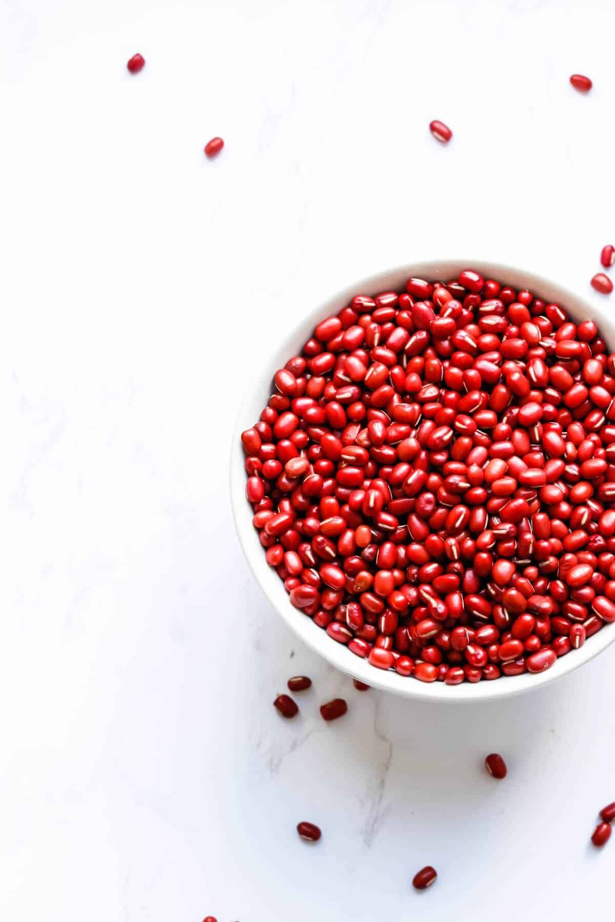 A white bowl filled with dried adzuki beans, some are scattered nearby.