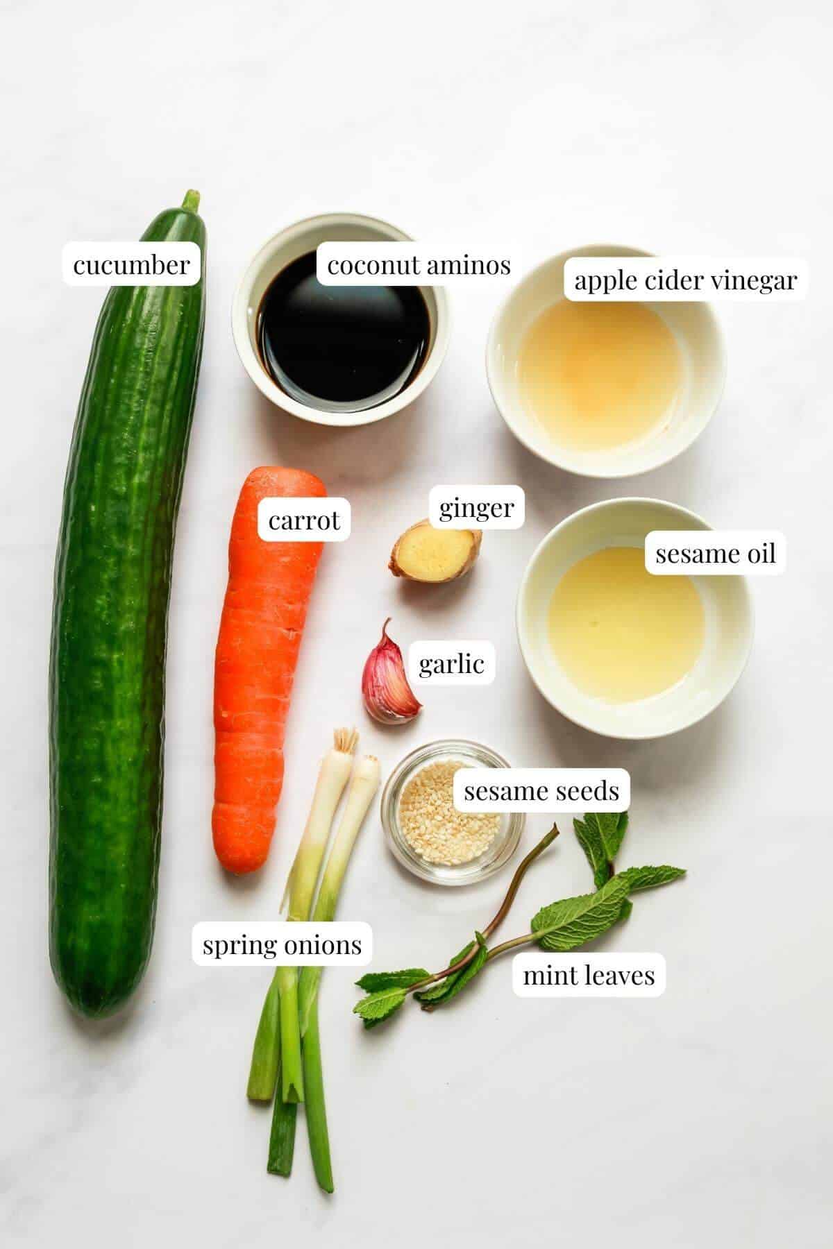 A white surface topped with cucumber and carrot salad recipe ingredients, each ingredient is labelled.