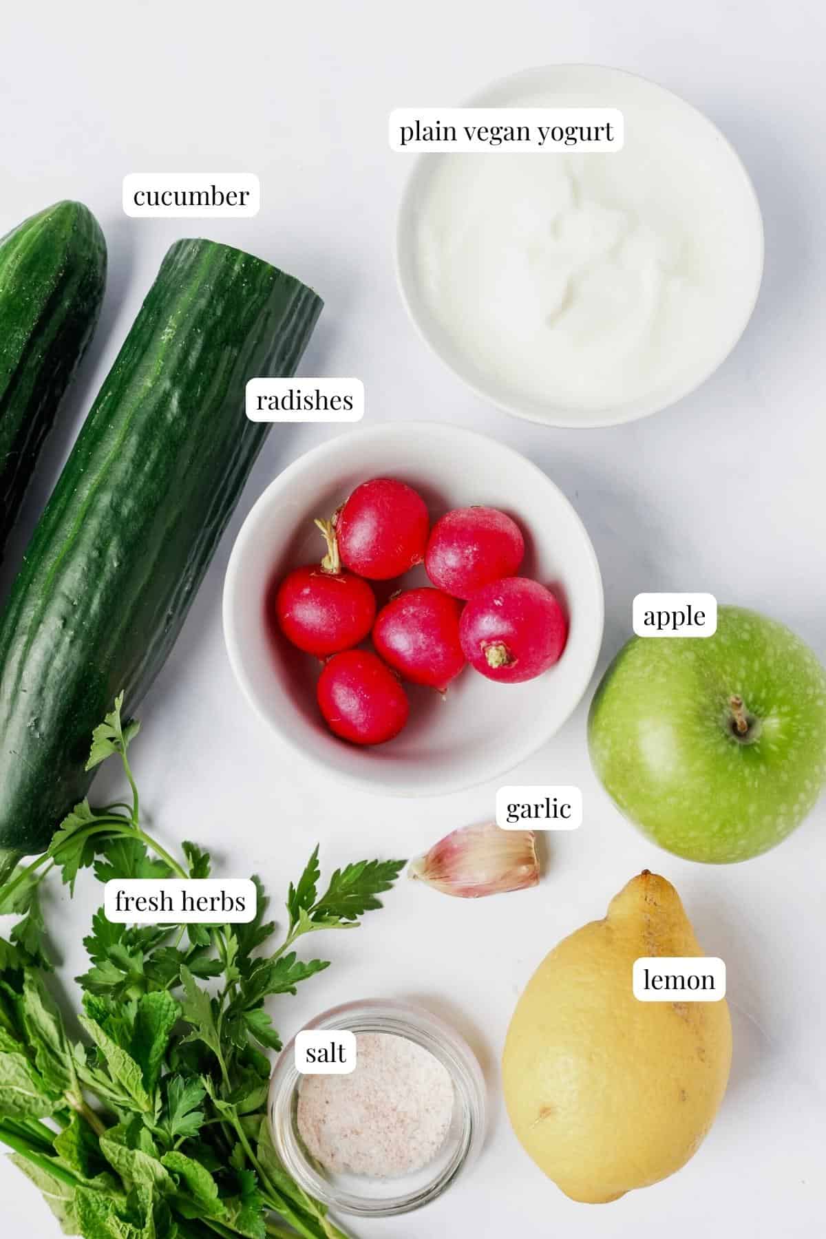 Recipe ingredients for a cucumber apple salad are laid out on a white surface and labelled.