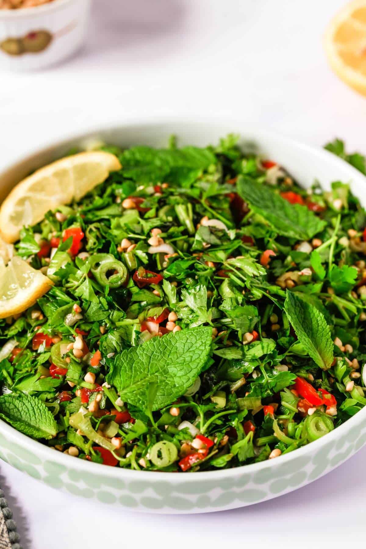 Close up of a bowl filled with finely chopped parsley salad, with buckwheat groats and tomatoes.