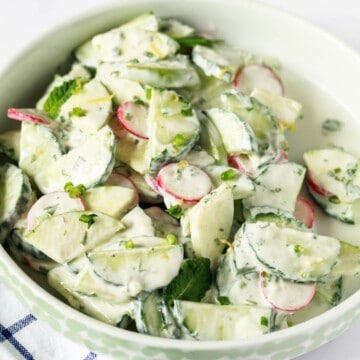 A close up image of bowl with cucumber apple salad in a white fresh herb dressing.