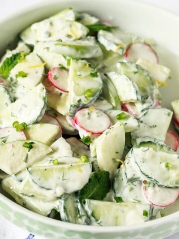 A close up image of bowl with cucumber apple salad in a white fresh herb dressing.