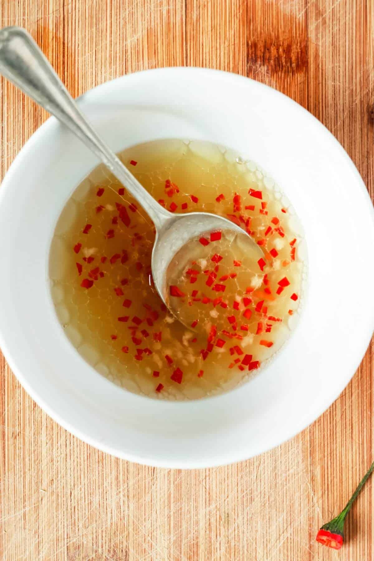 A silver spoon sitting in a bowl of salad dressing with finely chopped red chilli.