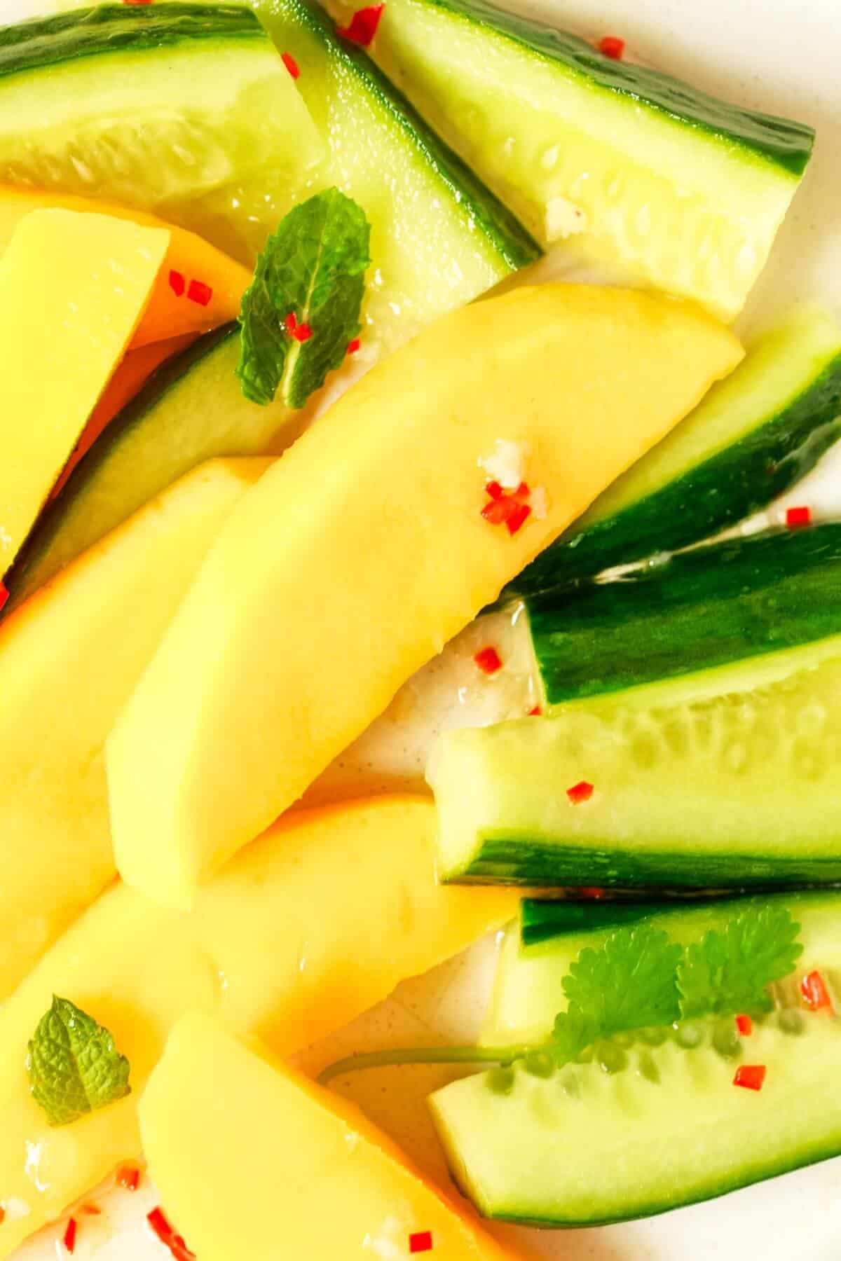 Close up of mango and cucumber slices, coriander, mint leaves and finely diced red chilli.