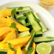 A plate of cucumber and mango slices, sprinkled with herbs and with half a fresh lime.