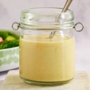 A small oopen topped jar filled with salad creamy dressing. A silver spoon sticks up out the top of the jar.