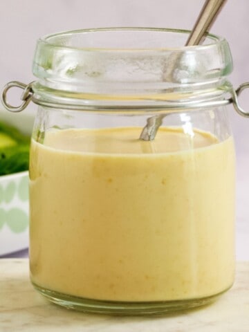 A small oopen topped jar filled with salad creamy dressing. A silver spoon sticks up out the top of the jar.