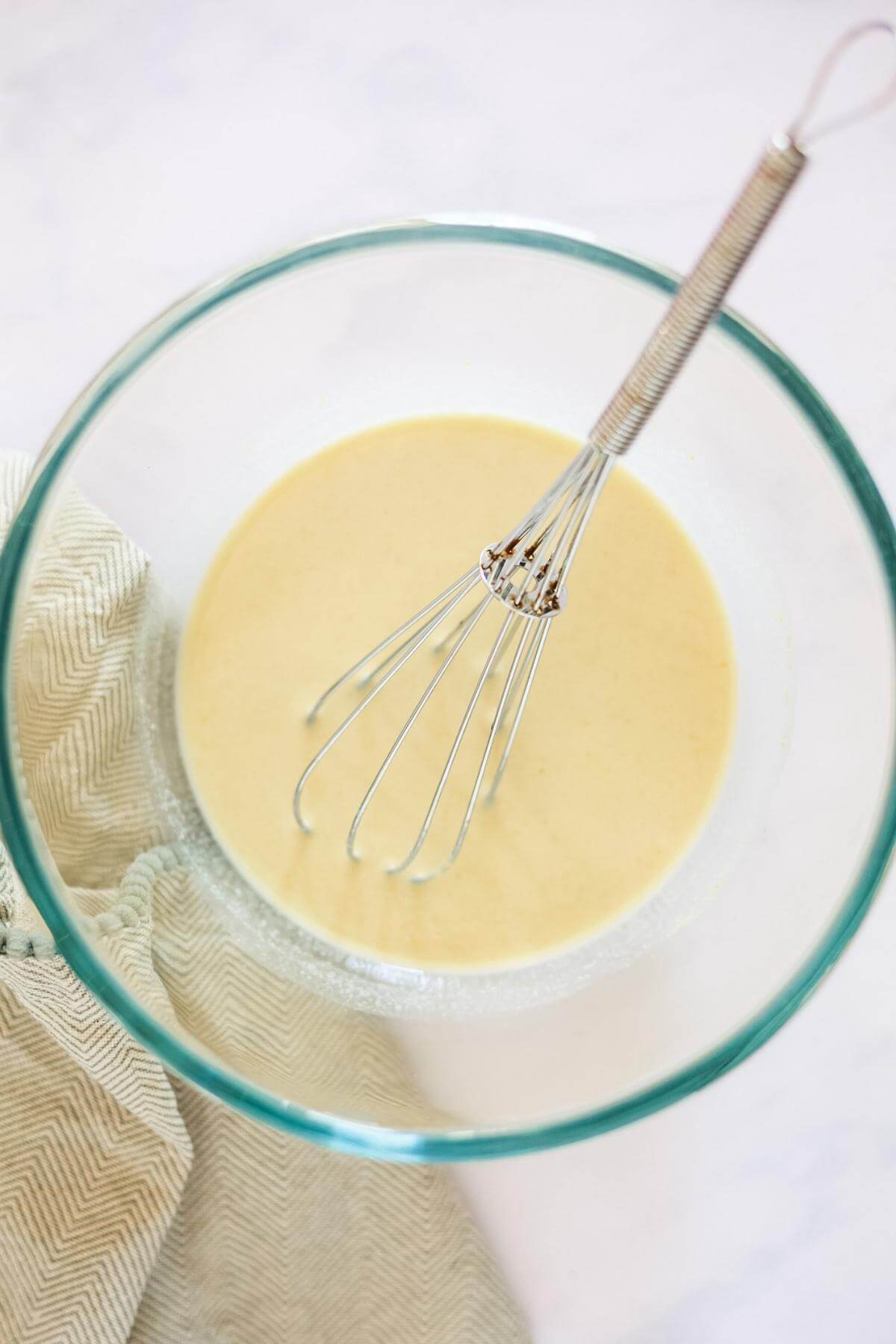 View from above of a small glass bowl containing cream sauce and a metal whisk.