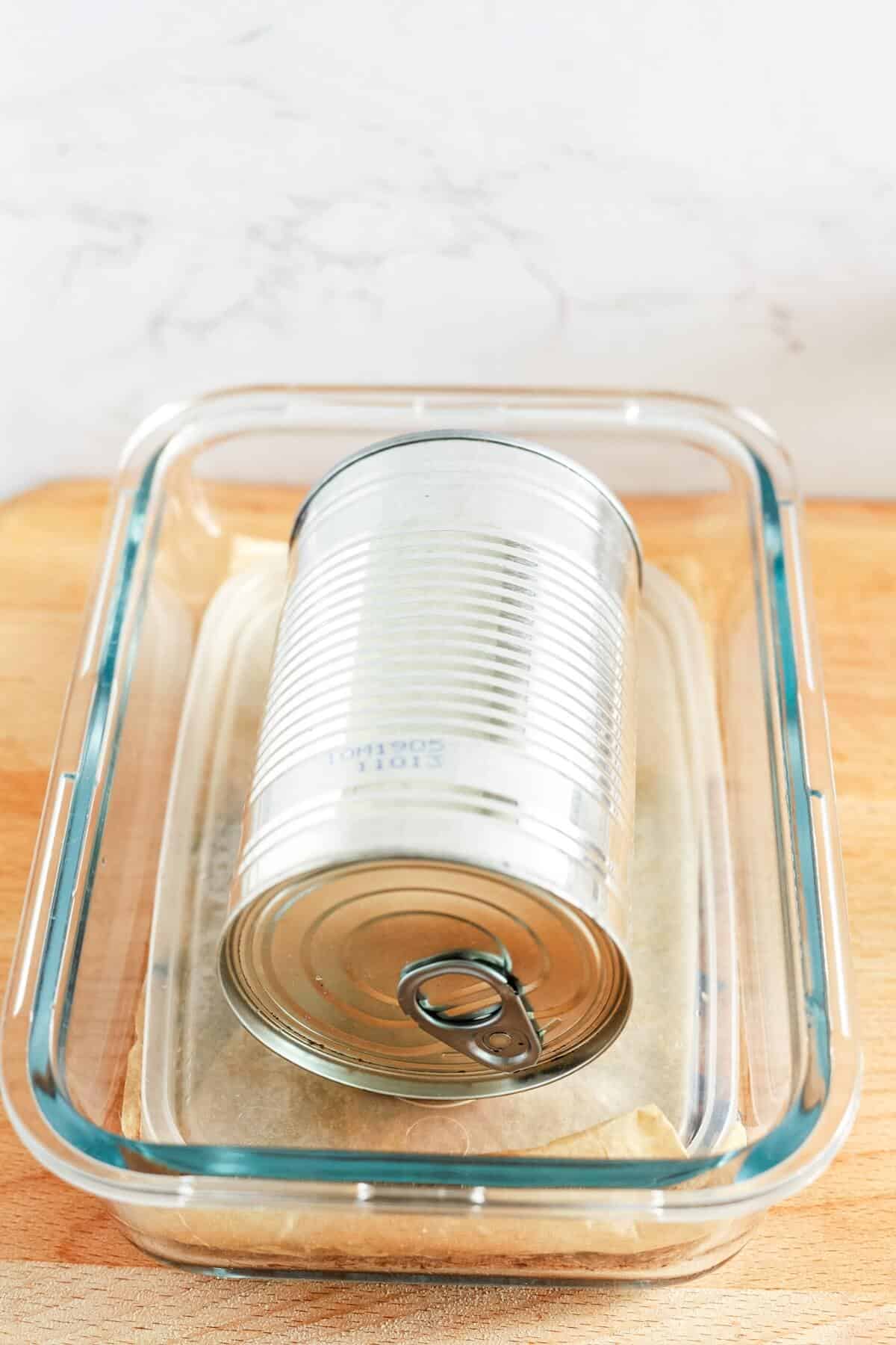 A tin can sitting on a plastic lid and inside a glass dish.