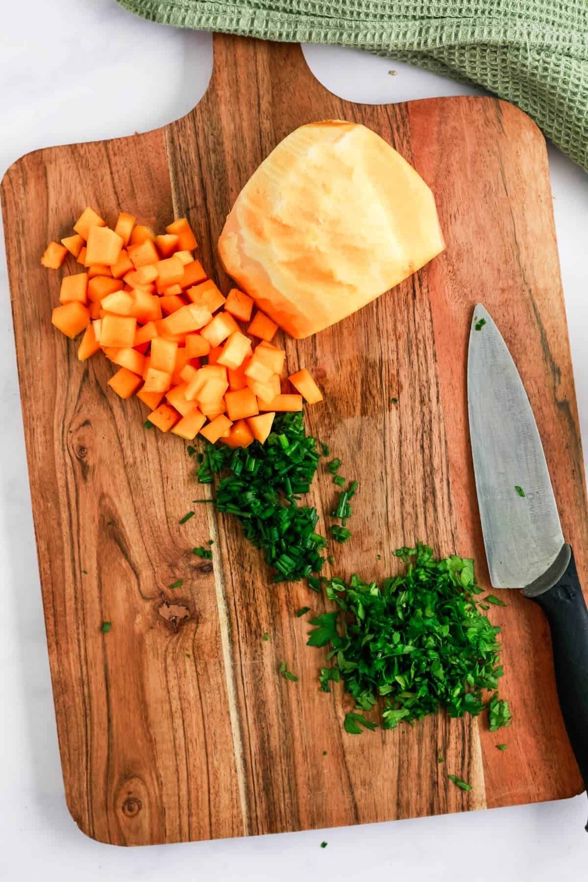 Chopped butternut squash and fresh herbs on a chopping board with a knife.