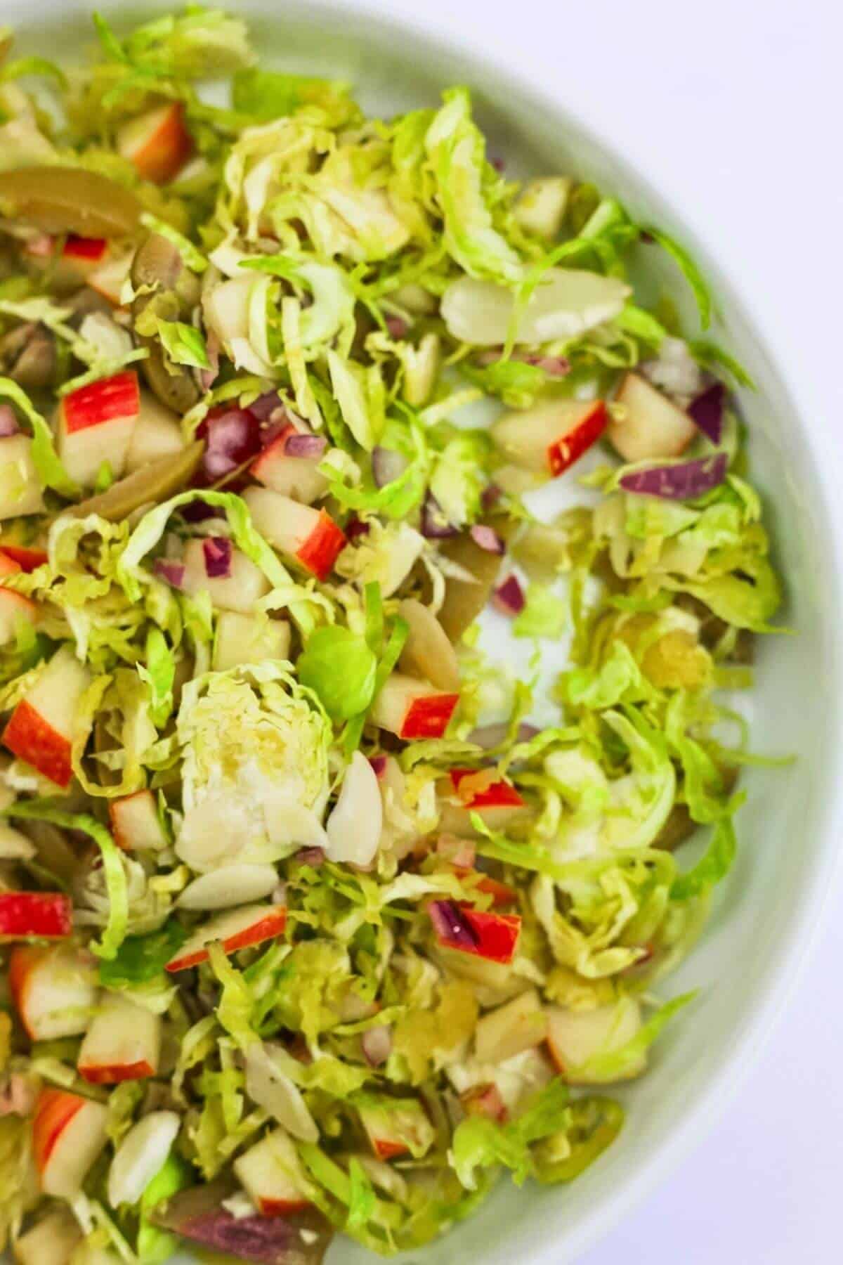 A salad with shredded greens and diced apple in a white ceramic bowl.